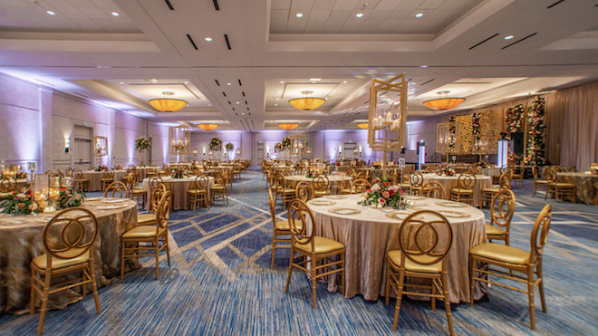 The ballroom at The Woodlands Waterway Marriott Hotel decorated for a reception with gold chairs and table decor. 